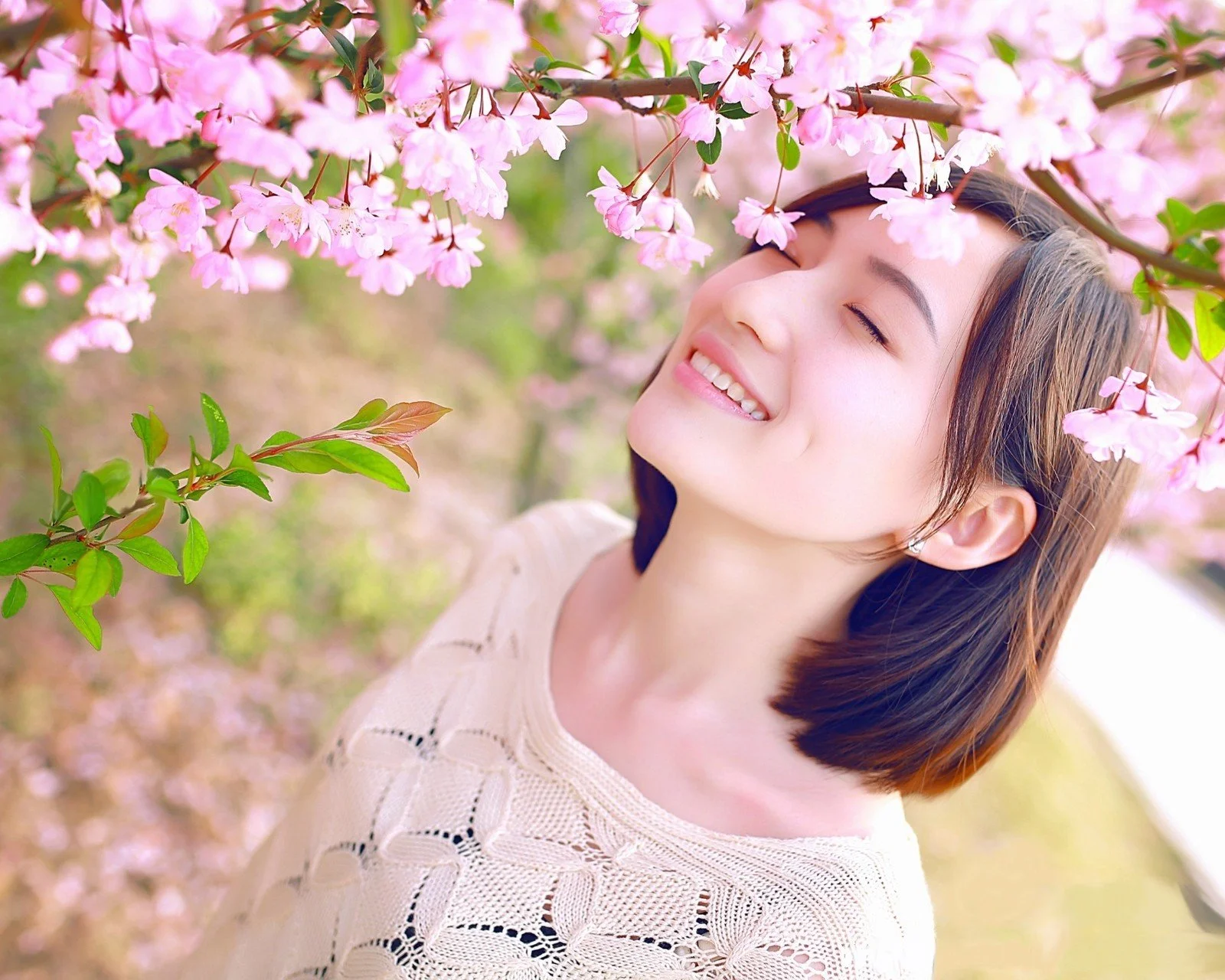 一位成年女子在盛开的粉色樱花枝下闭眼微笑。