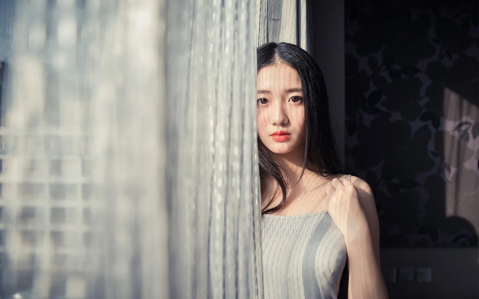一名女性站在半透明窗帘后，光线映照出她的面容与身影。