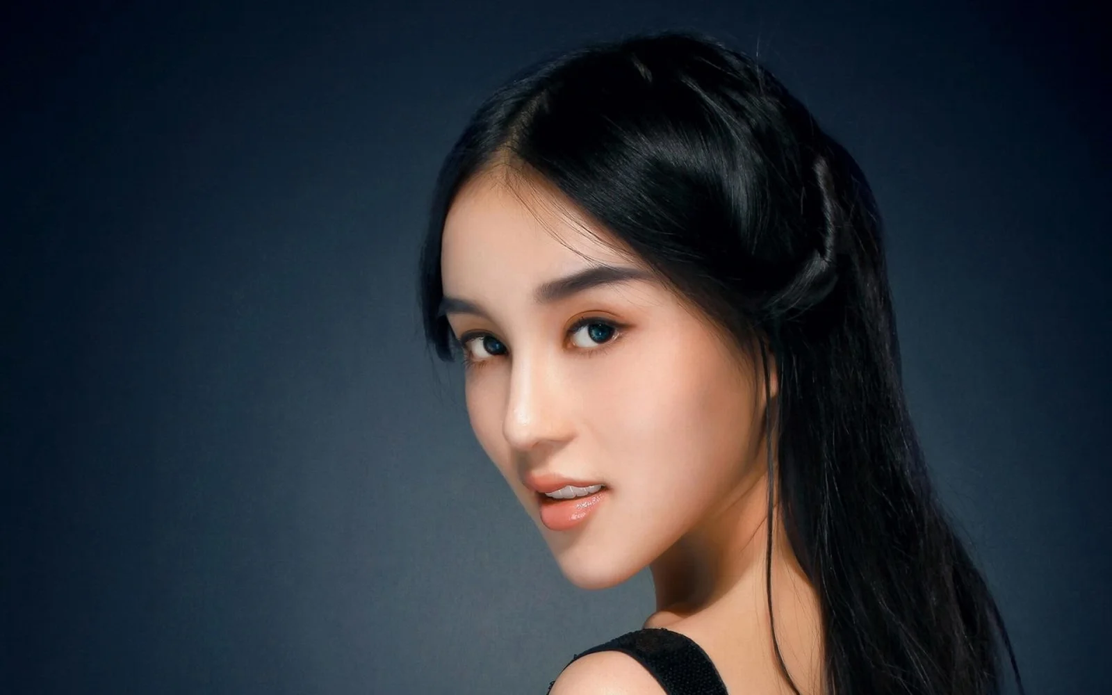 一位黑发女性在深色背景前侧身凝视镜头。