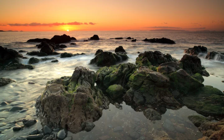 夕阳映照下的海面与布满岩石的海岸构成宁静的自然风景。