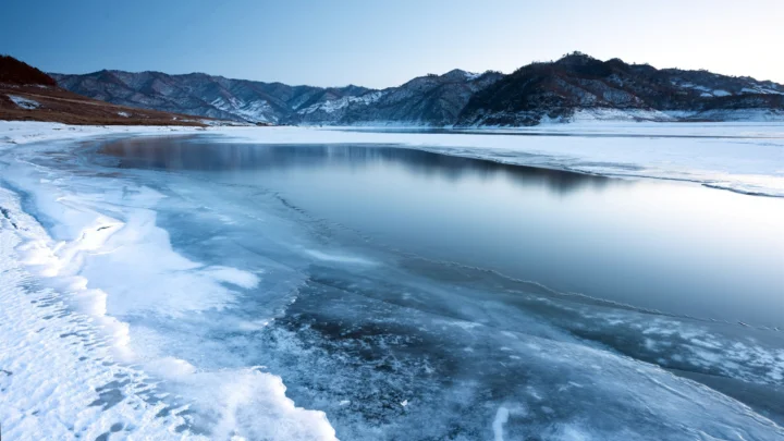 冰雪覆盖的湖面延伸至远处群山之间，呈现宁静的冬日景色。