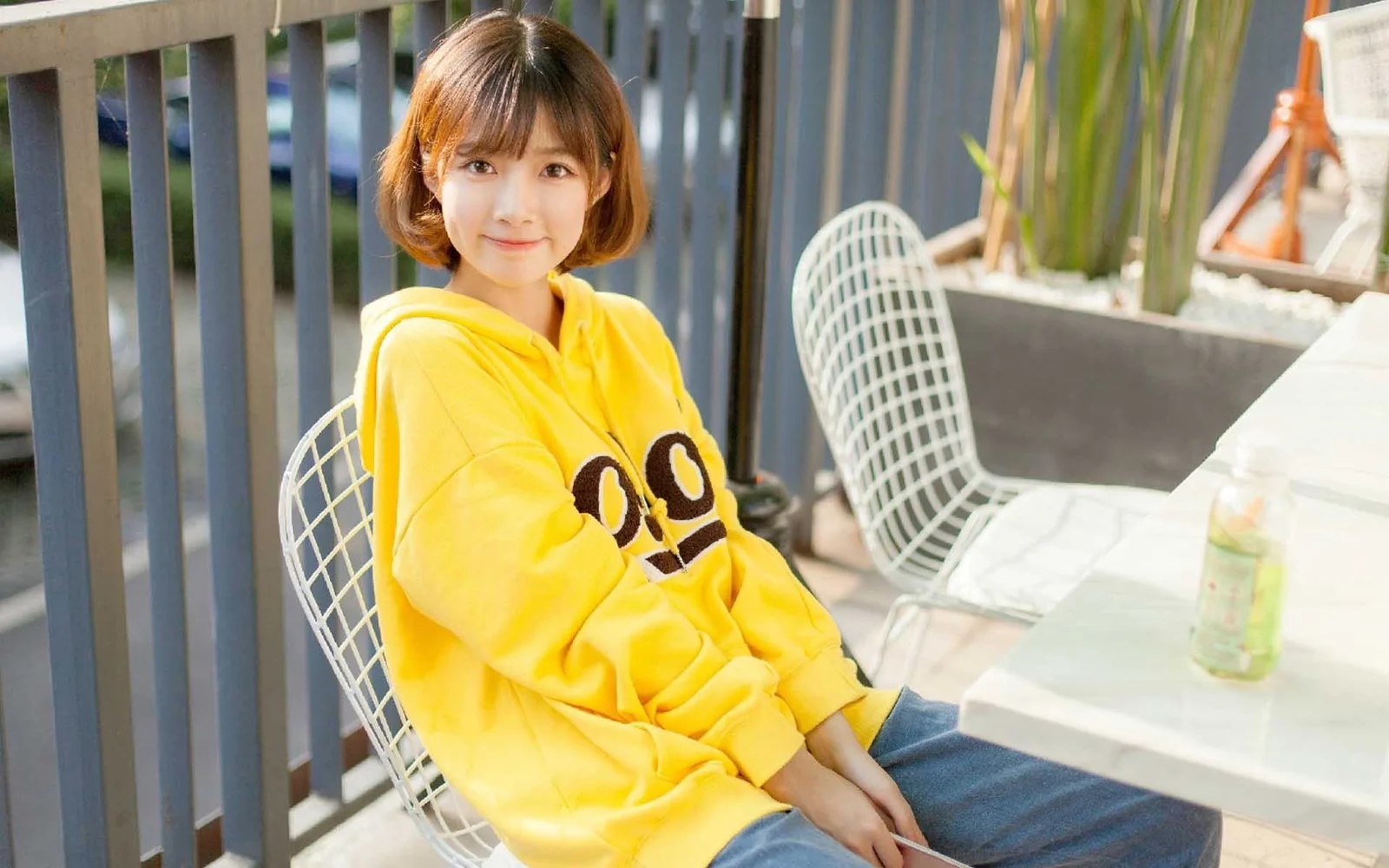노란색 후드티를 입은 여성이 밝은 테라스 의자에 앉아 있습니다.