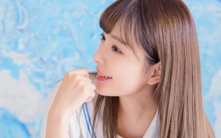 一位长发女性侧身望向一侧，手靠近嘴边，蓝色背景衬托出清新的肖像画面。