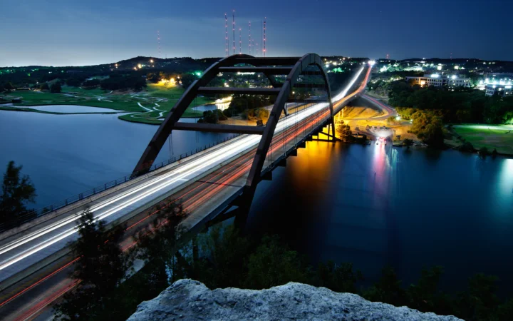 夜幕下的拱桥横跨湖面，车流形成明亮的光轨，远处城市灯火闪烁。