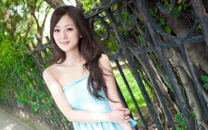 一名成年女子站在户外树木和藤蔓旁微笑面对镜头。