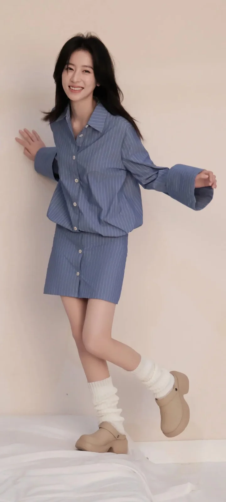 파란색 줄무늬 의상을 입은 미소 짓는 여성이 밝은 실내 배경 앞에서 포즈를 취하고 있습니다.