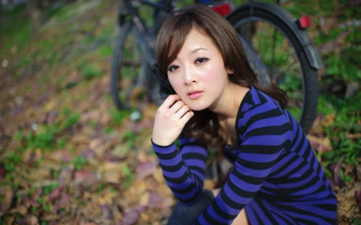 一名身穿蓝黑条纹上衣的成年女性在户外自行车旁看向镜头。