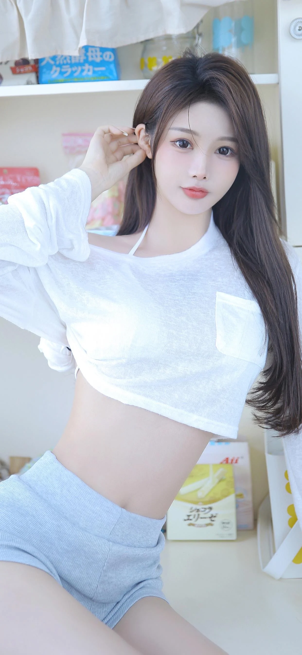 一名长发女性身穿白色上衣和浅色短裤，在室内面对镜头摆姿势。