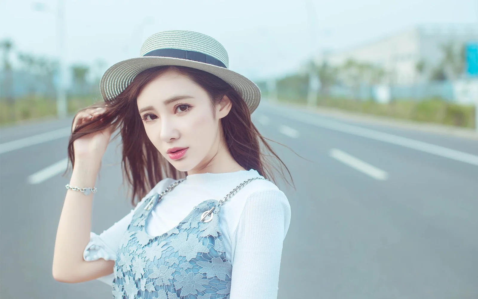 一名戴着宽檐帽的女性站在公路旁，背景是开阔的道路与模糊的户外景色。