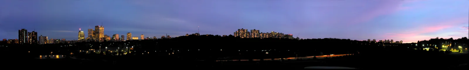 해질 무렵의 도시 스카이라인이 지평선을 따라 펼쳐지고 건물의 불빛이 어두운 풍경을 밝힌다.