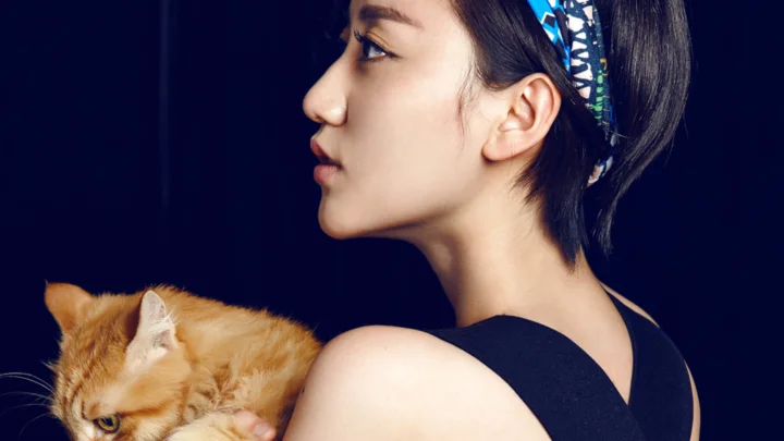 一名成年女性侧脸抱着一只橘猫，背景为深蓝色。