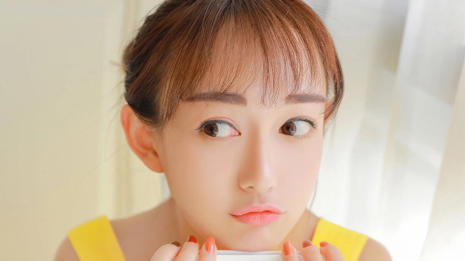 一位棕发女子穿着黄色上衣，以近距离肖像呈现在浅色背景前。