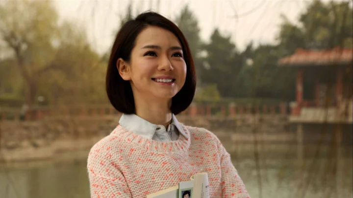 一位微笑的成年女性站在池塘边，手中拿着一本小册子。