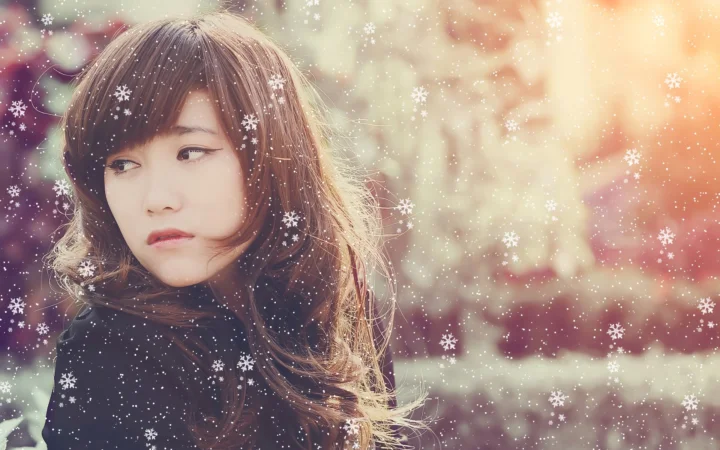 一位棕色长发女子在飘雪的冬日户外侧目凝望。