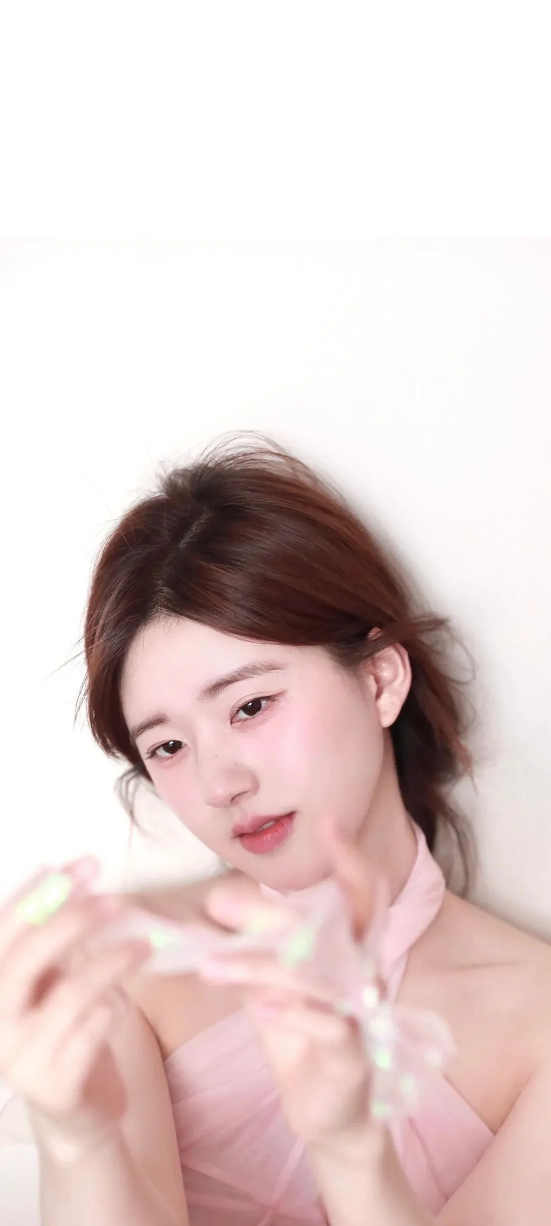 一位成年女性身穿粉色上衣，近距离面对镜头，手中拿着一串浅色装饰物。