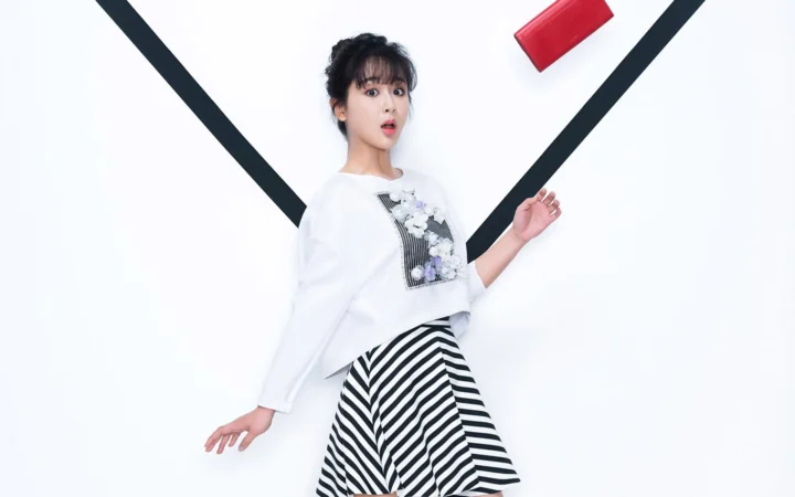 一名成年女性身穿白色上衣和黑白条纹裙站在白色背景前。