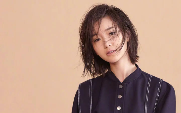 一位成年女性身穿深色衬衫，在暖色背景前面对镜头。
