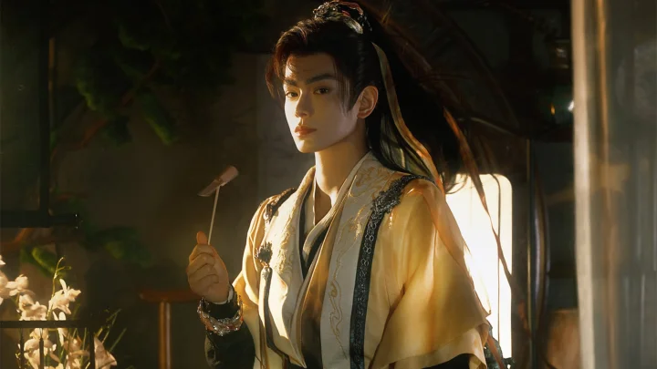 一名长发男子身穿传统服饰，在温暖的室内光线下手持小物件。