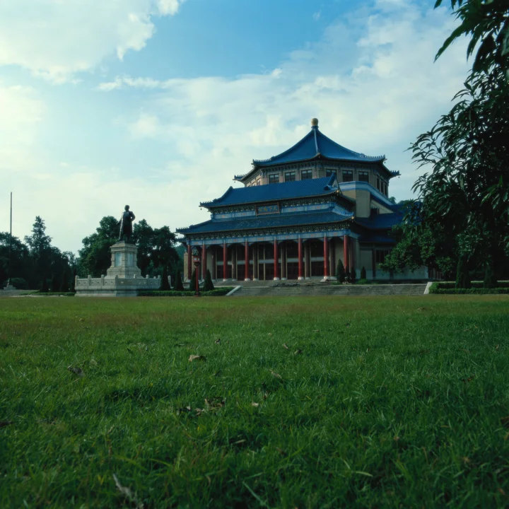 一座蓝色屋顶的中式建筑坐落在开阔的绿草坪旁，天空中飘着白云。