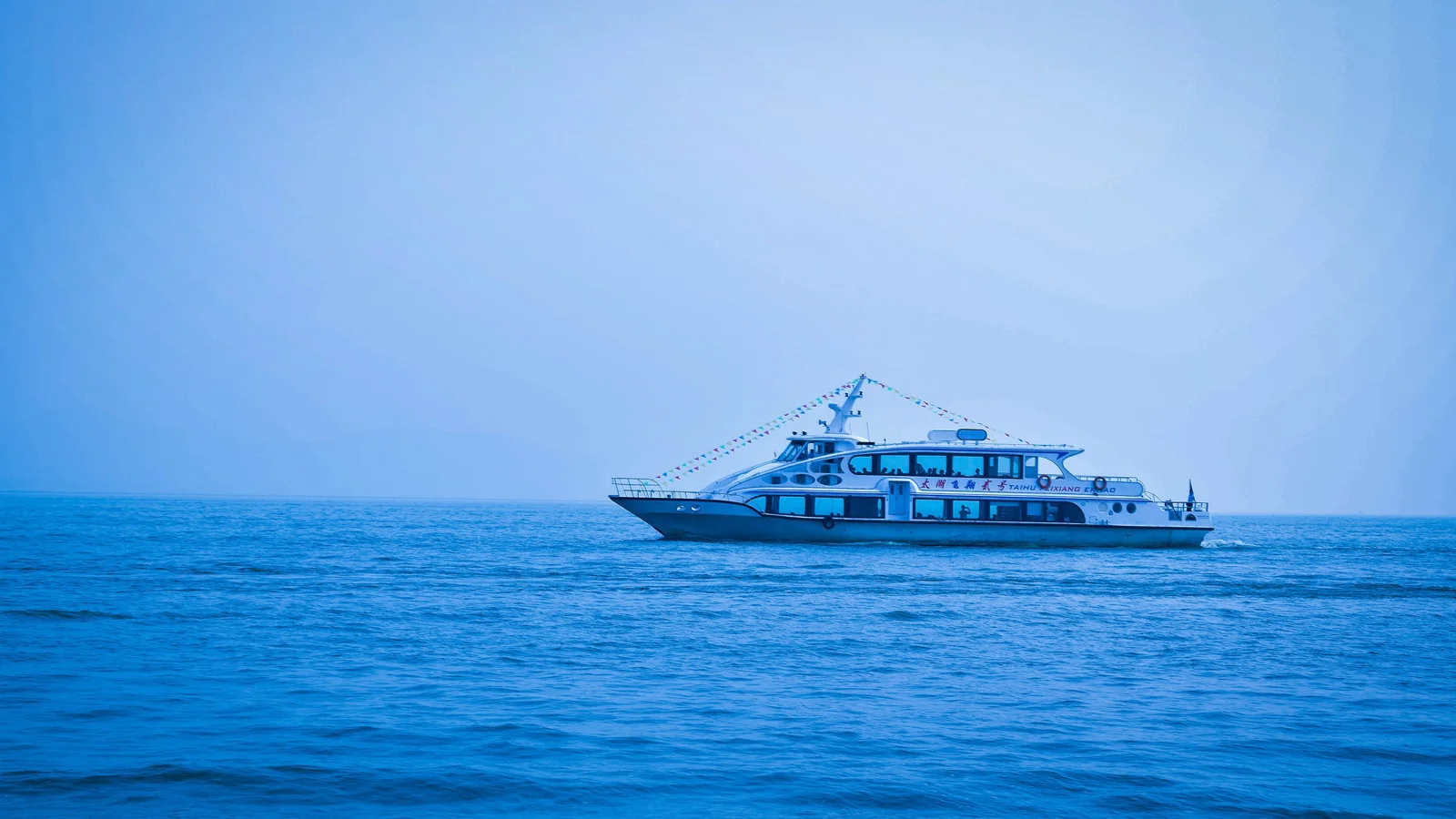 青い海の上を白い船が進み、遠くに広い空が広がっています。