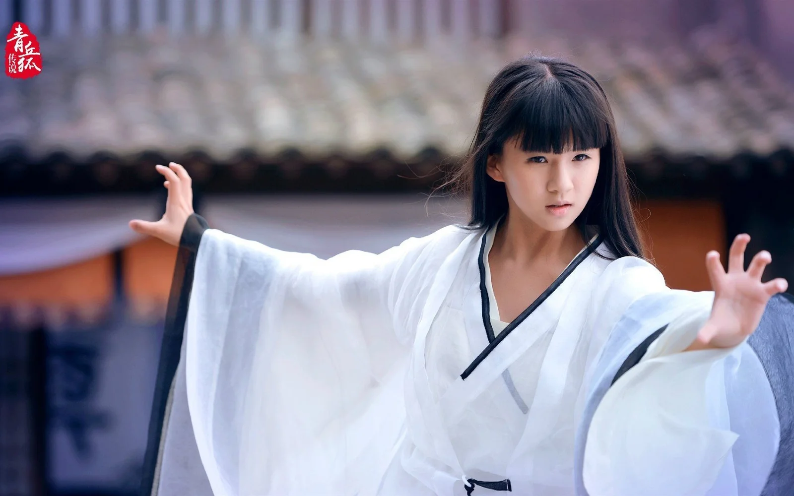 一名穿白色宽袖衣服、留黑色长发的女性在模糊背景前伸展双臂。