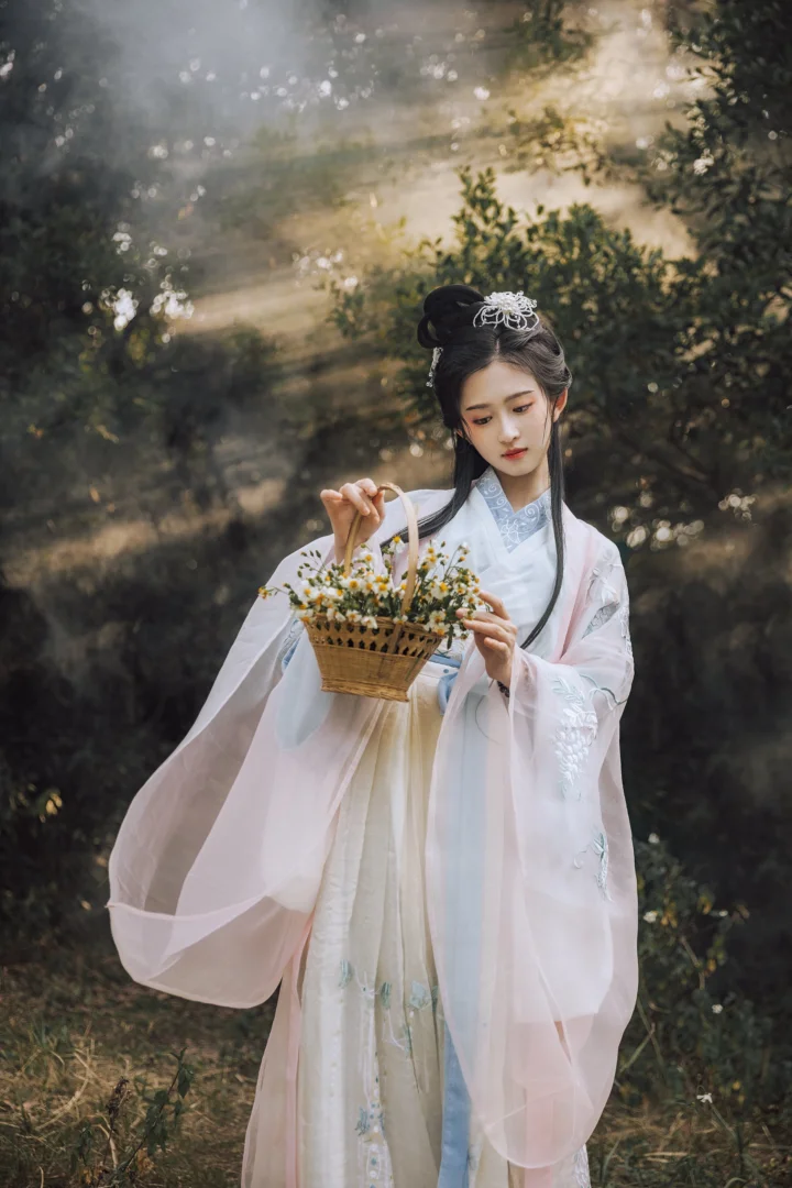 一位身穿浅色传统服饰的女子站在森林中，手提装满小花的篮子。