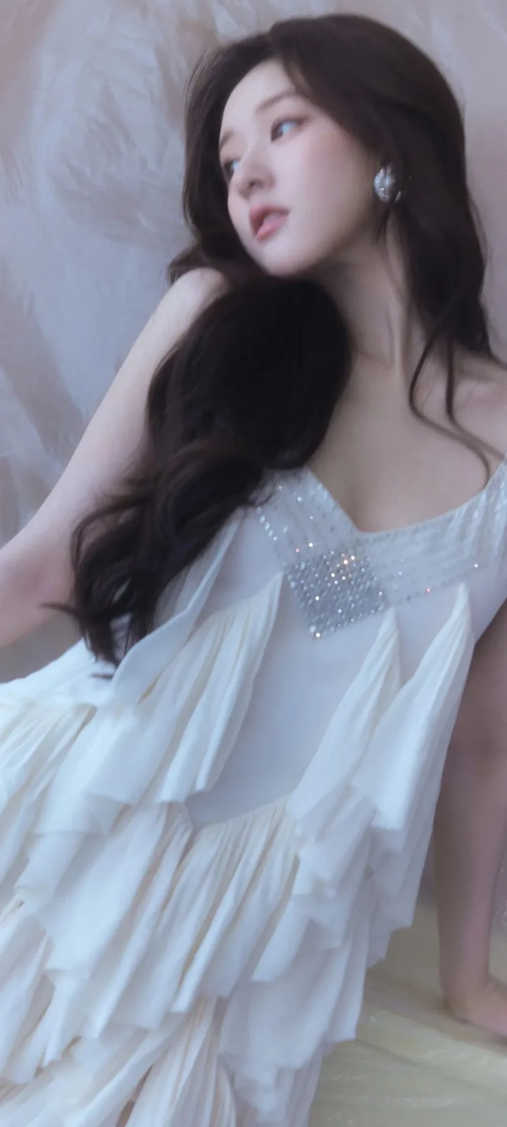 一名长发女子身穿白色连衣裙靠坐在室内。