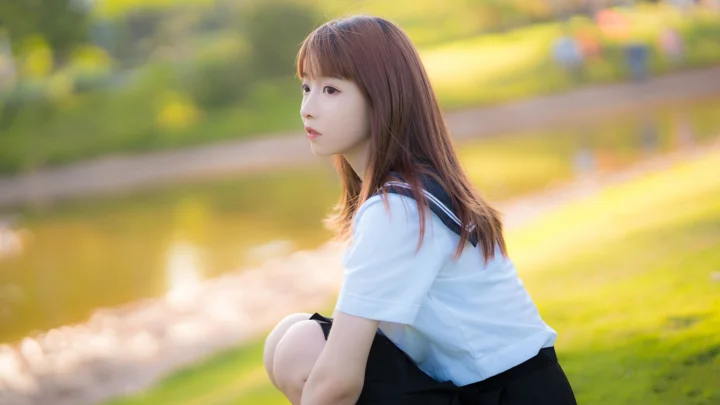 一名长发女子坐在阳光柔和的公园草地旁。