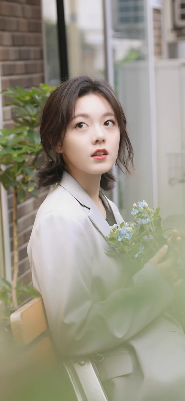 一名女性在城市建筑旁的窗边手持一束浅蓝色花朵。