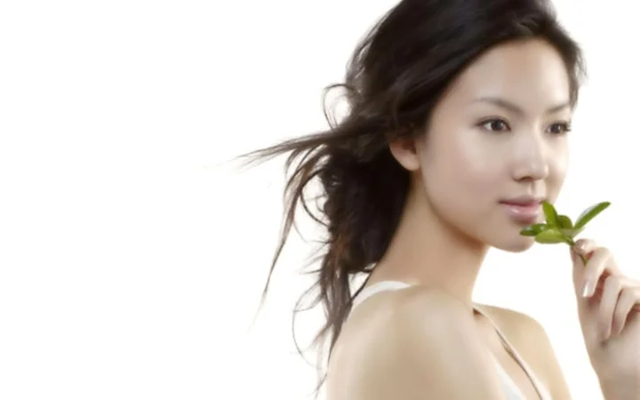 흰색 배경 앞에서 성인 여성이 작은 잎가지를 들고 옆모습을 보이고 있습니다.