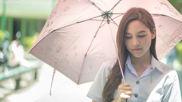 一名年轻女子在户外撑着一把浅粉色雨伞。