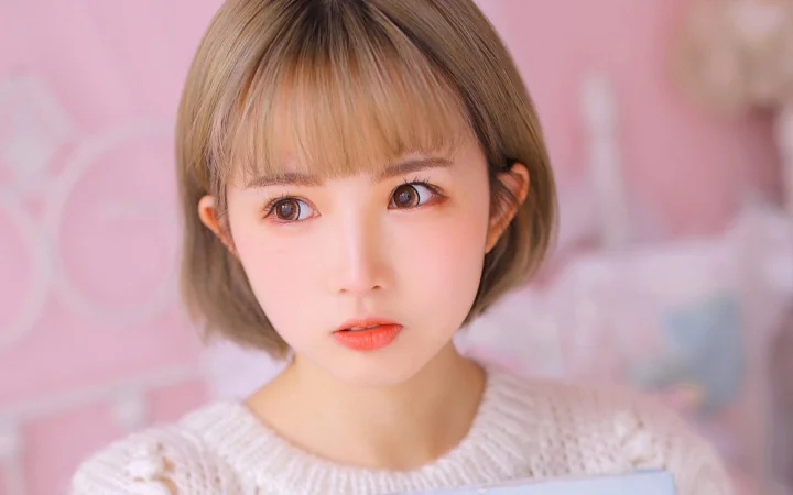 一位短发女性在粉色背景前面向镜头。