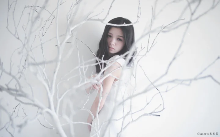 一名穿白衣的女子站在蒼白的枝條之間。
