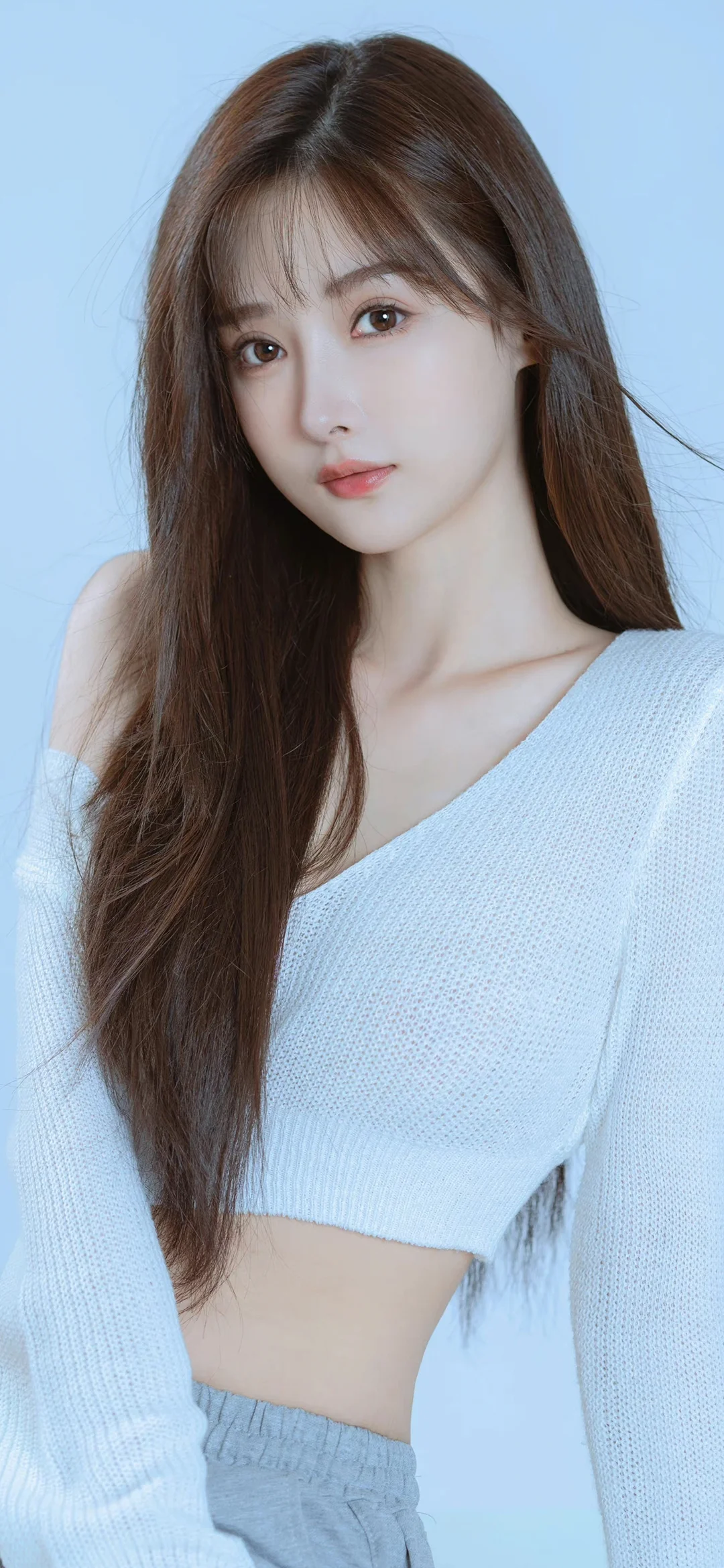 一名长发女性穿着浅蓝色针织毛衣，在浅蓝背景前面对镜头。