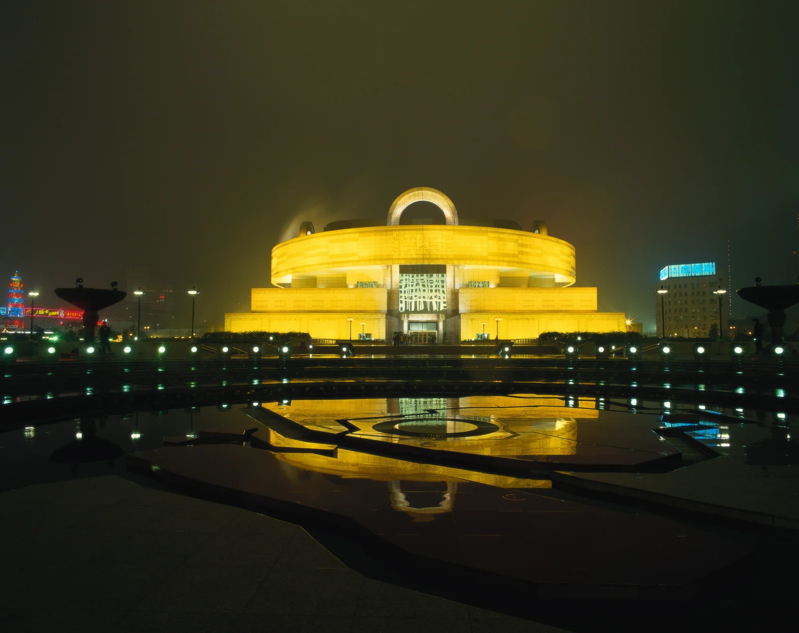 夜晚灯光映照下的城市建筑倒映在广场水面上。