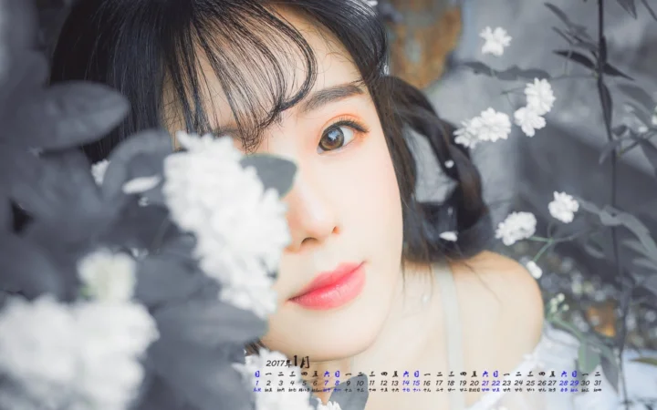 一位成年女性的近距离人像被灰色叶片和白色花朵环绕，底部可见日历文字。