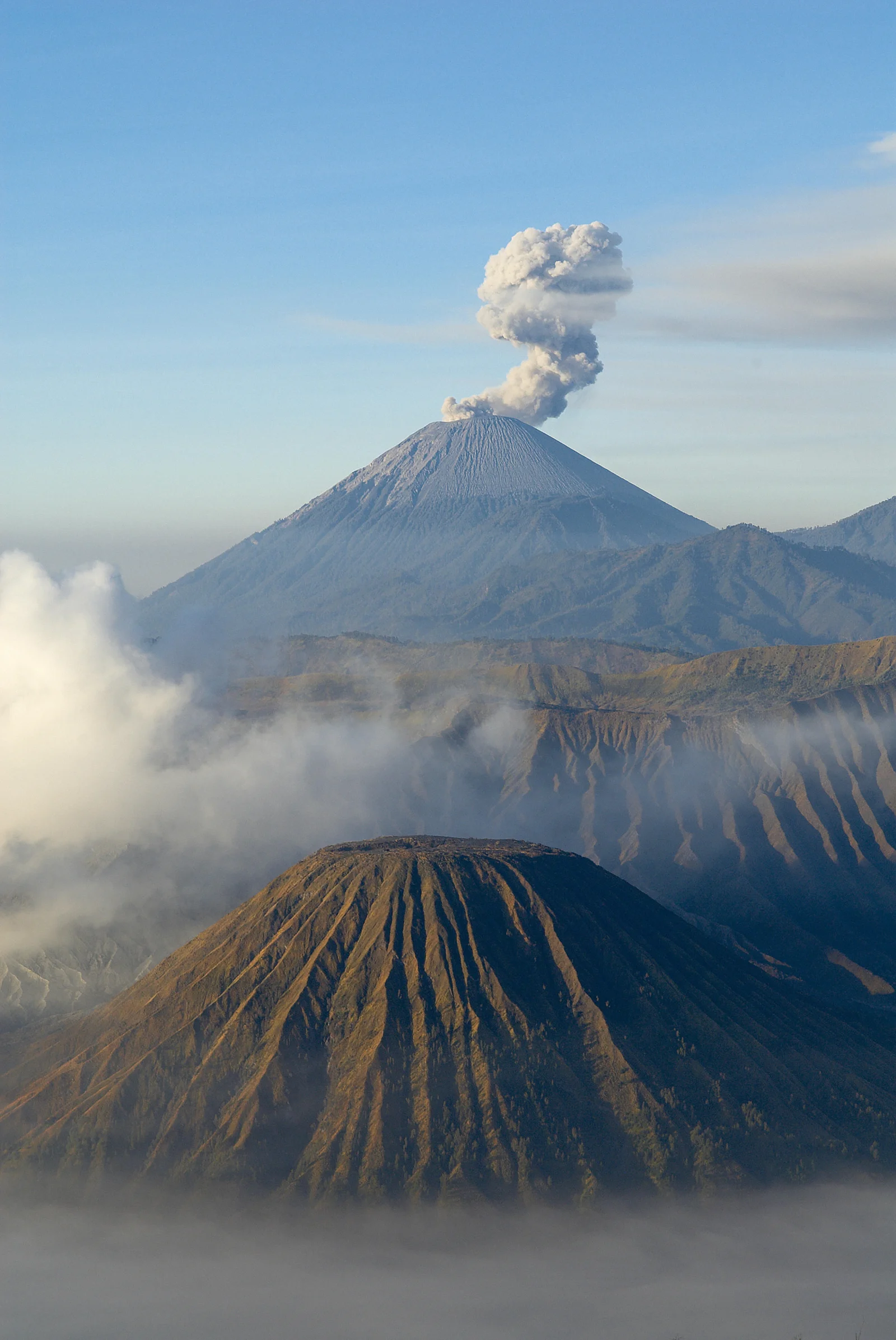 一座冒着白色烟雾的火山矗立在群山与云雾之间。