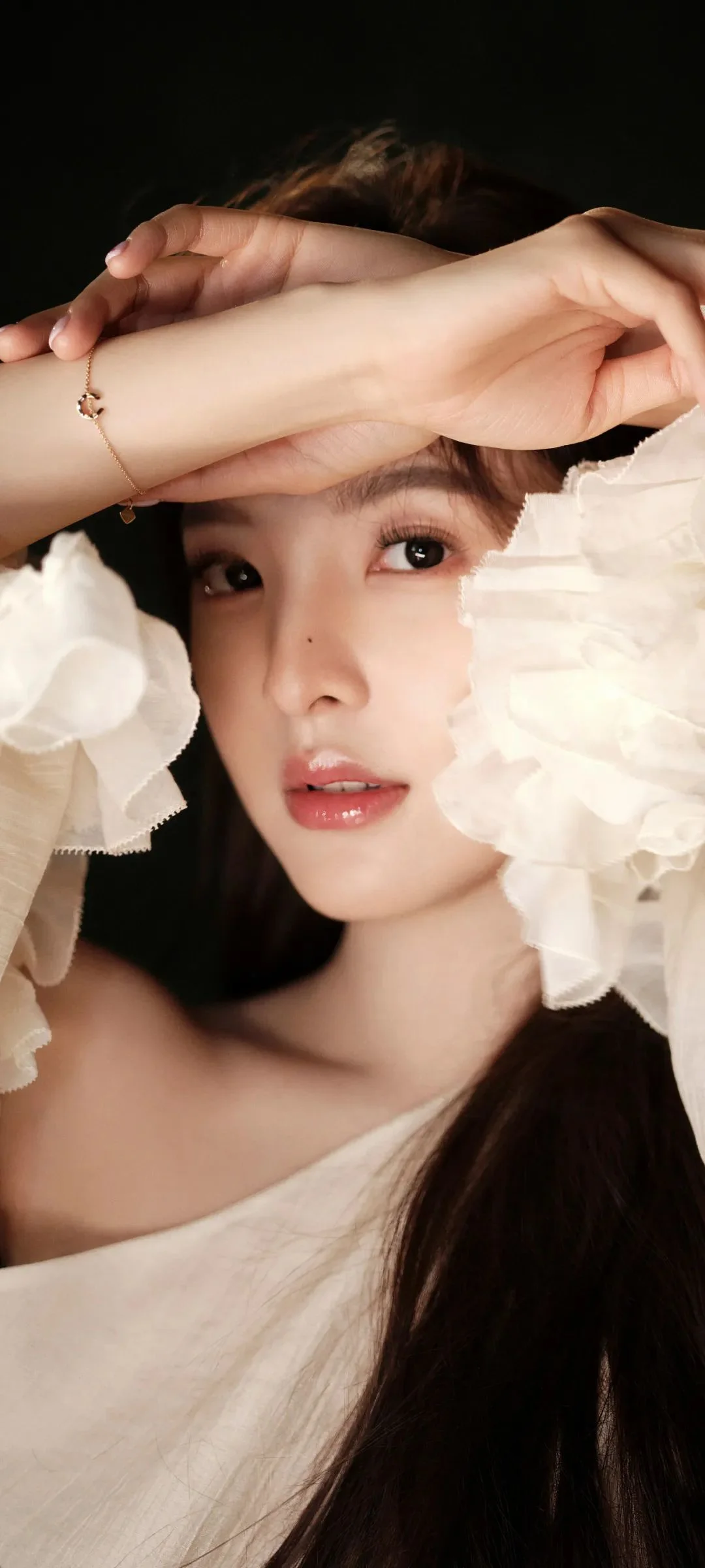 한 여성이 카메라를 바라보며 이마 앞에 팔을 올리고 있고 얼굴 주변을 흰색 프릴 소매가 감싼 근접 인물 사진이다.