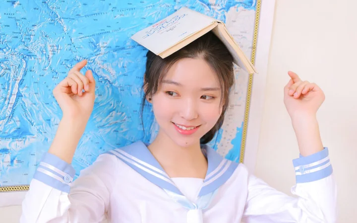 一名身穿白色水手领上衣的微笑女性靠在蓝色地图前，头上放着一本书。