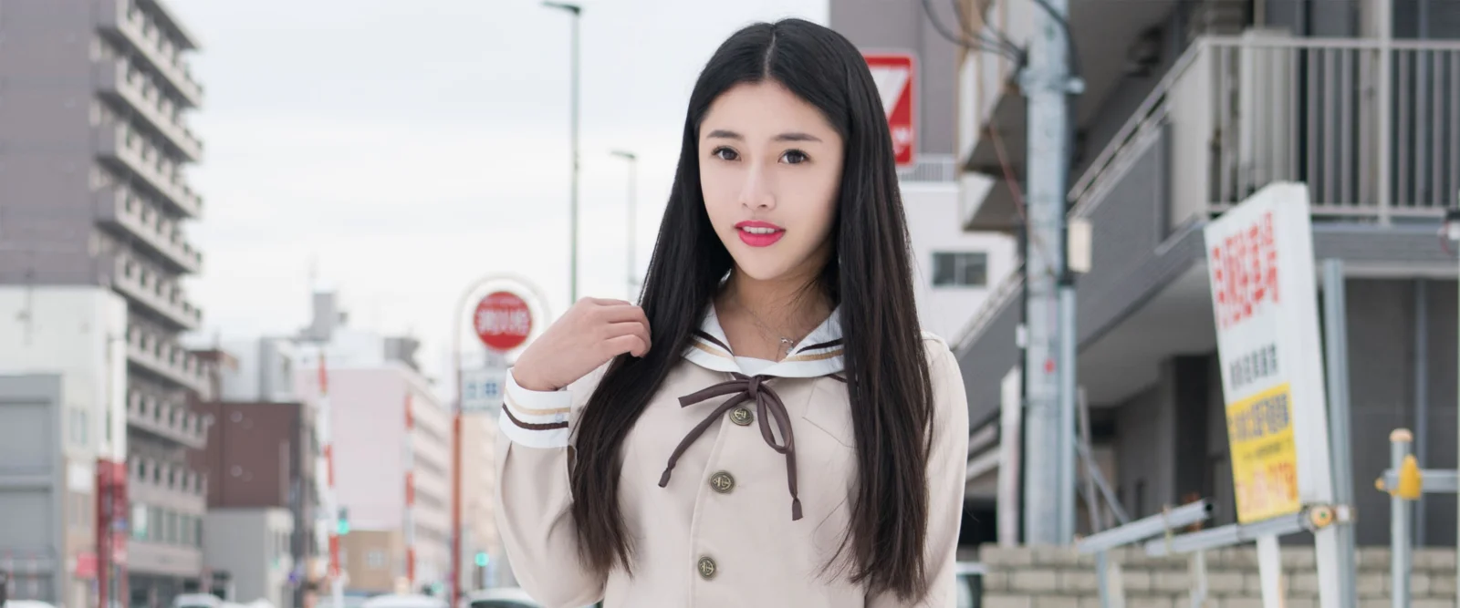 一名黑色长发女子站在城市街道上，身后可见建筑和街道设施。