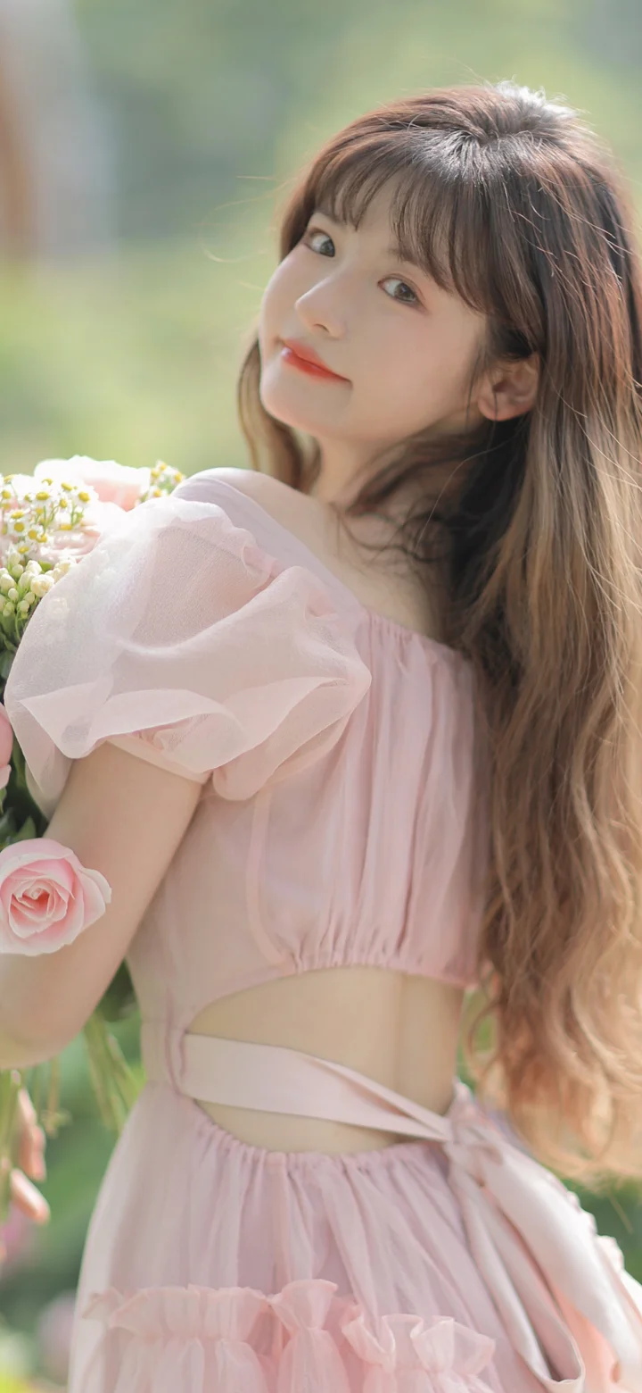 ピンクのドレスを着た女性が屋外で花束を手に振り返っている。