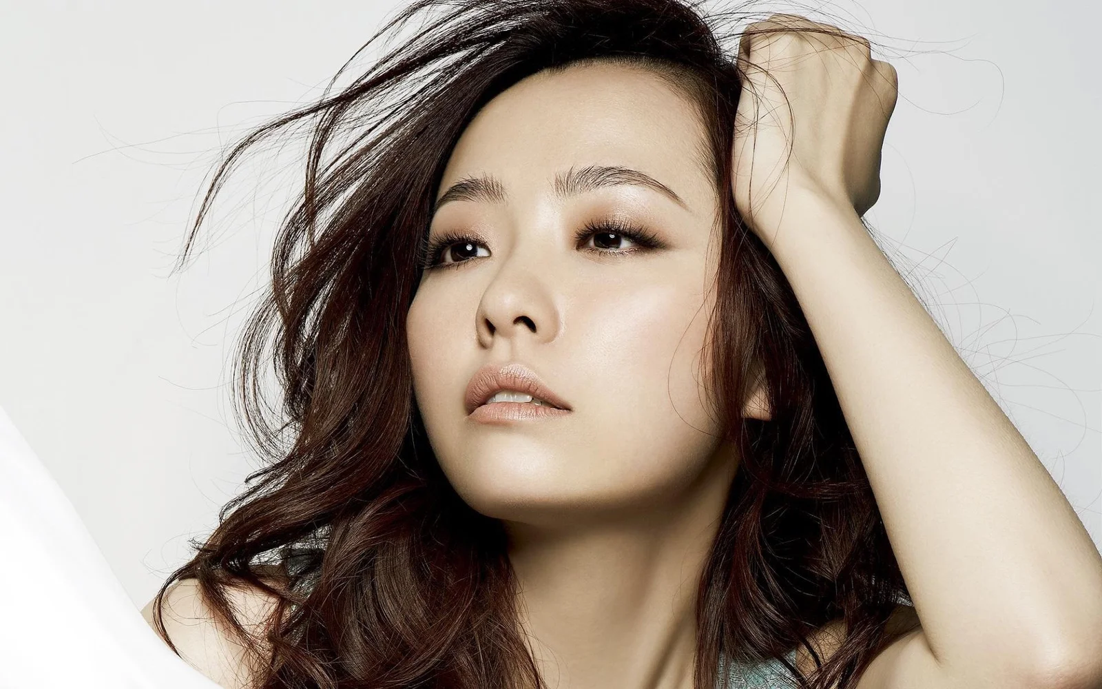 一名成年女性以近距离肖像呈现，长卷发披散，手臂抬至头侧。