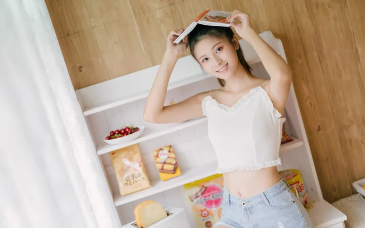 一名女性在室内举着书本，站在木质墙面和置物架前。
