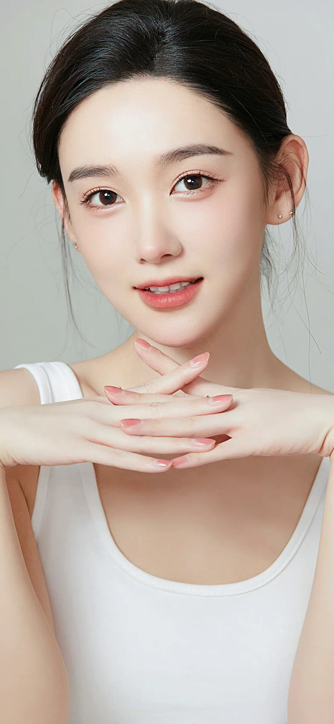 白いタンクトップを着た成人女性が、胸元で手を重ね、カメラに向かって微笑んでいる。