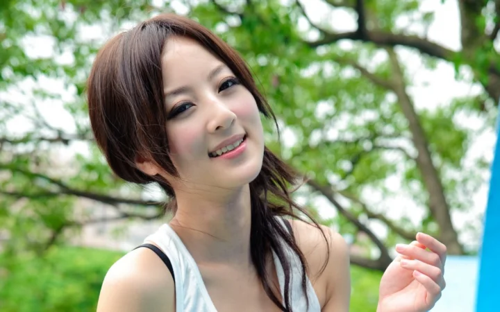 미소 짓는 여성이 나무를 배경으로 카메라를 바라보고 있습니다.
