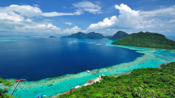 航拍视角下，湛蓝海水、绿色群岛、珊瑚礁与晴朗天空构成壮丽的海洋风景。