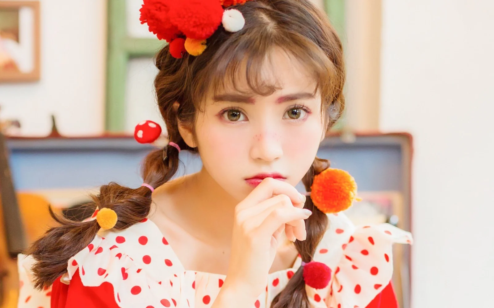 땋은 머리에 물방울무늬 옷을 입은 여성이 실내에서 카메라를 바라보고 있습니다.