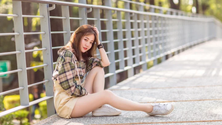 一名年轻女子坐在阳光照耀的桥面上，身后是延伸的金属栏杆。