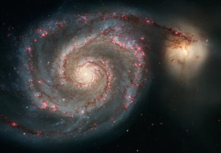 A spiral galaxy with a bright companion, red star-forming regions, and a dark star field.
