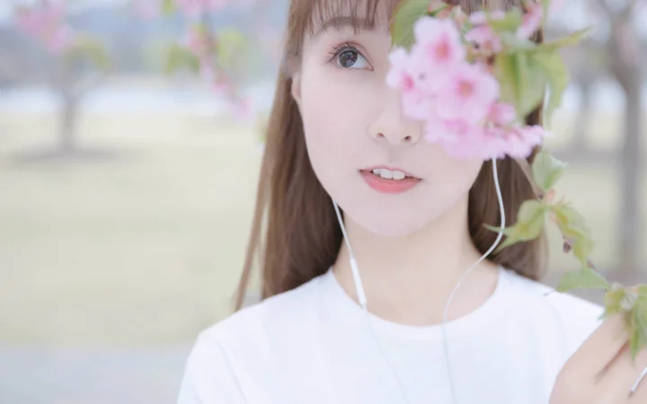 一名戴着耳机的女性在户外樱花旁微笑注视镜头。